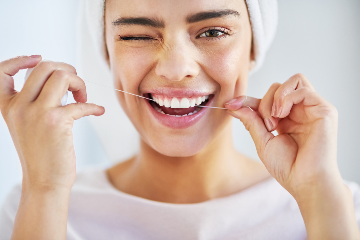 A woman flossing her teeth and winking