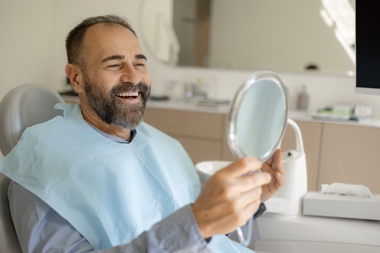 man smiling into hand mirror after LANAP procedure