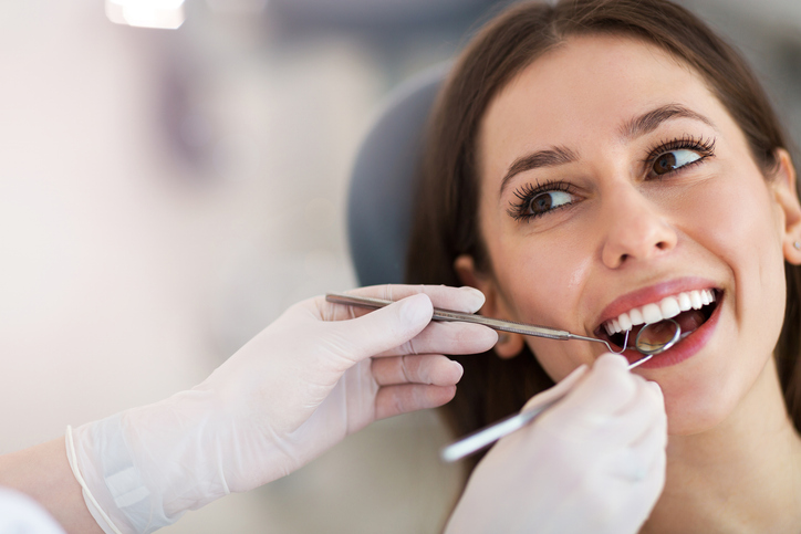 happy female dental patient in dental chair dentist holding dental tools