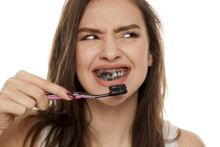 young woman brushing her teeth with charcoal toothpaste.