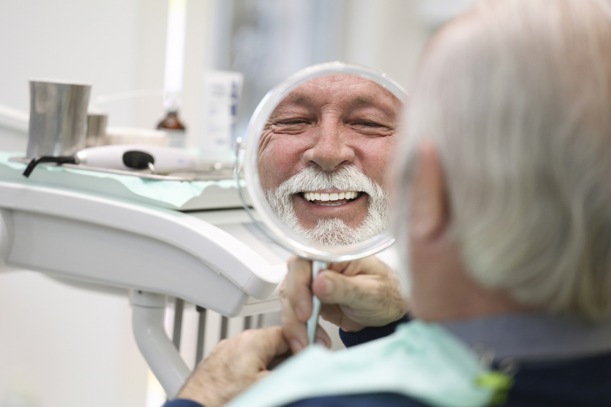 senior male dental implant patient smiling in mirror